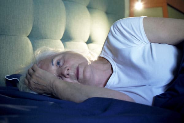 A woman lies awake in bed with insomnia, which is one of many common sleep disturbances in older adults.