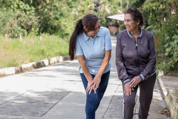 A woman tries to encourage an older adult to exercise regularly by going on regular walks outside together.
